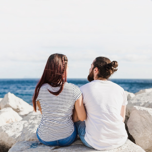 Foto gratuita pareja sentada en rocas por el mar