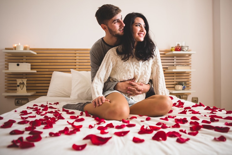 Foto gratuito pareja sentada de rodillas en una cama con pétalos