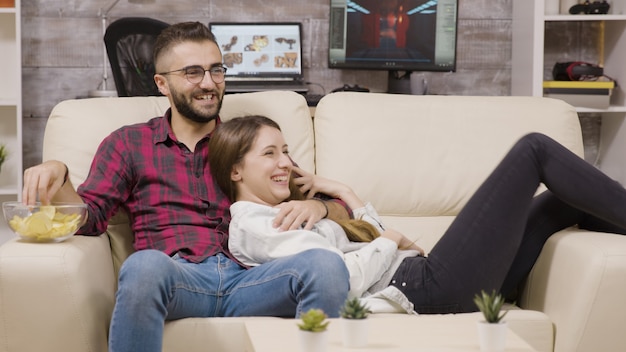 Pareja sentada en el sofá y riendo mientras ve la televisión.