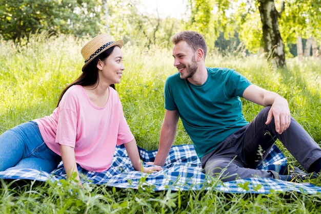 Foto gratuita pareja sentada en tela escocesa en picnic