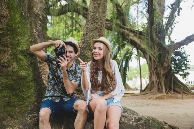 Pareja sentado en raíz de árbol haciendo una foto