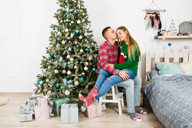 Pareja en silla al lado de árbol de navidad