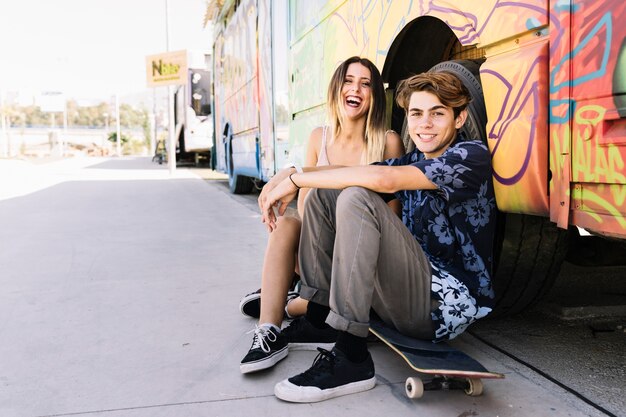 Pareja skater riendo apoyados contra un autobús