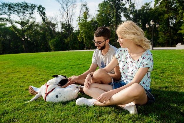 Pareja sonriendo, sentado en el césped con bulldog francés en el parque