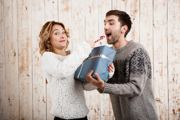 Pareja sonriendo sosteniendo dulces y regalos de Navidad sobre pared de madera