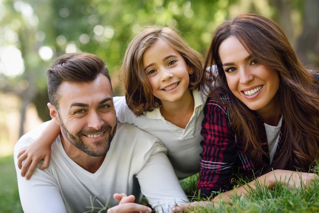 Pareja sonriendo tumbada en el césped con su hija