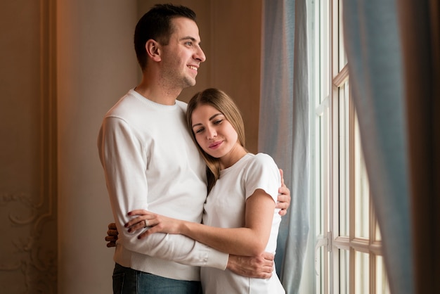 Pareja sonriente abrazada junto a la ventana