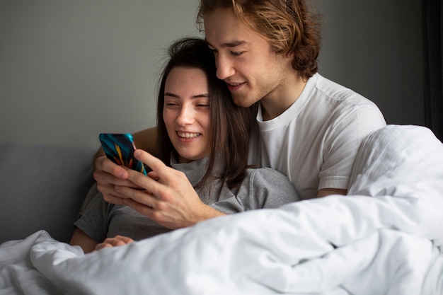 Foto gratuita pareja sonriente abrazados mientras mira a los teléfonos inteligentes