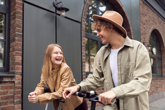 Foto gratuita pareja sonriente al aire libre en la ciudad con scooters eléctricos