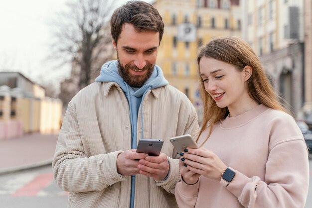 Pareja sonriente al aire libre en la ciudad con teléfonos inteligentes