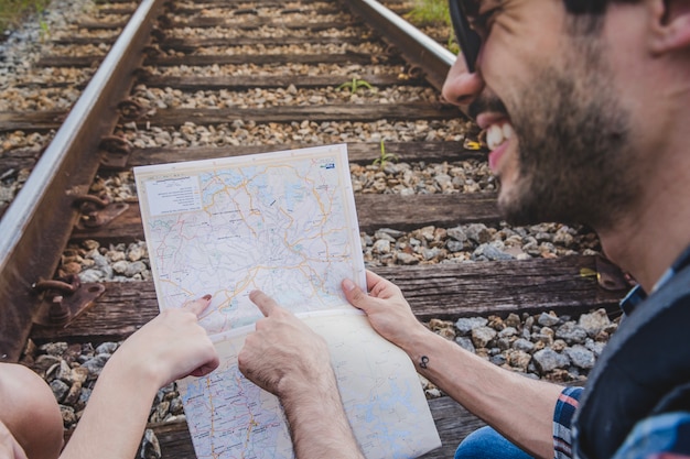 Pareja sonriente apuntando a mapa en vías de tren