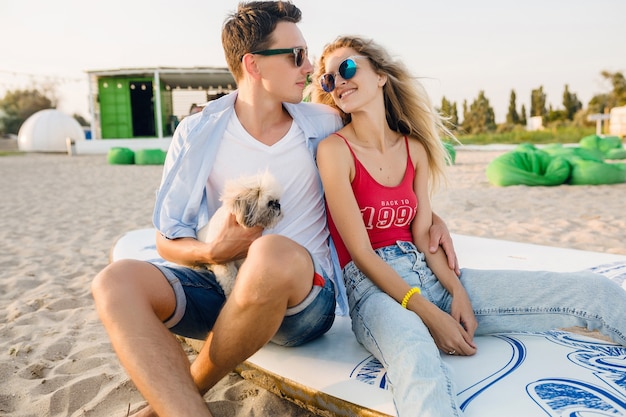 Pareja sonriente atractiva joven divirtiéndose en la playa jugando con perro