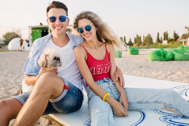 Pareja sonriente atractiva joven divirtiéndose en la playa jugando con perros de raza shih-tsu