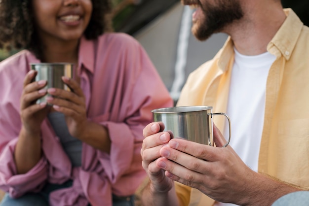 Pareja sonriente con bebidas calientes mientras acampa al aire libre