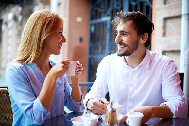 Pareja sonriente bebiendo café y mirándose el uno al otro