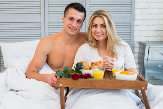 Pareja sonriente en la cama cerca del desayuno a bordo