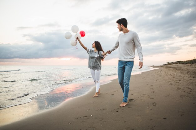 Pareja sonriente caminando por la playa con globos