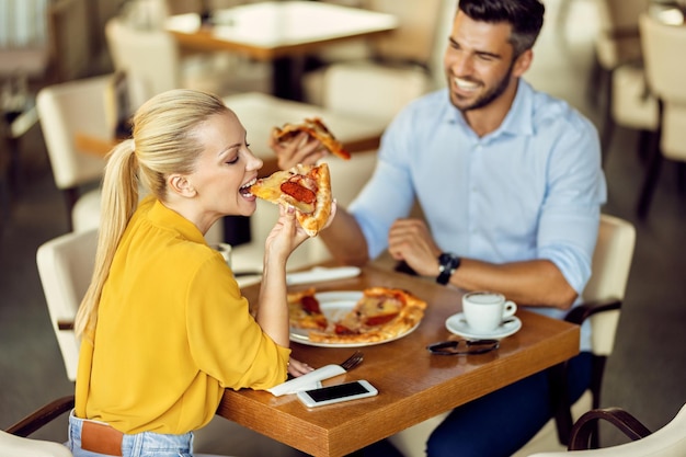 Pareja sonriente comiendo pizza para almorzar en un restaurante