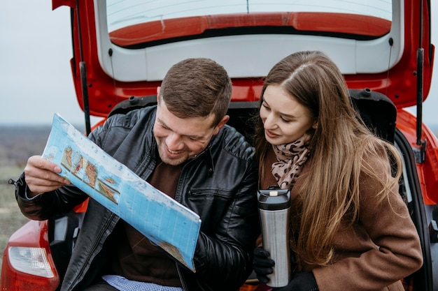 Pareja sonriente comprobando un mapa en el maletero del coche