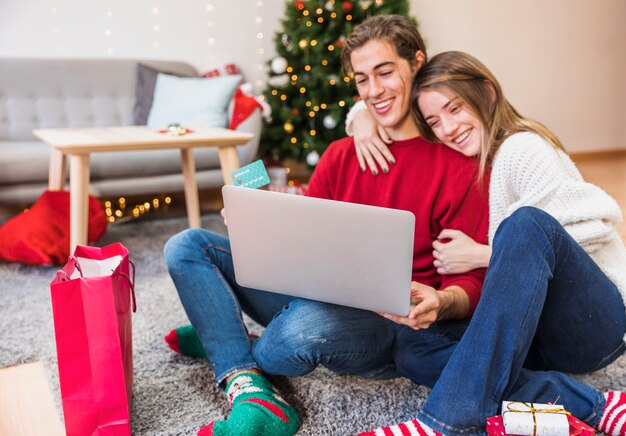 Pareja sonriente con la computadora portátil en el piso