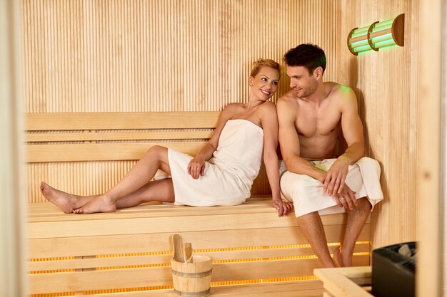 Pareja sonriente comunicándose mientras está sentado en la sauna en el spa de salud