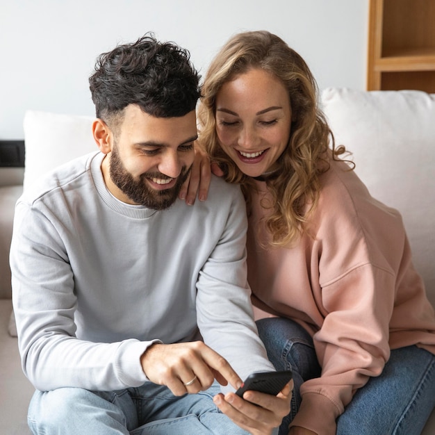 Pareja sonriente demandando smartphone en casa