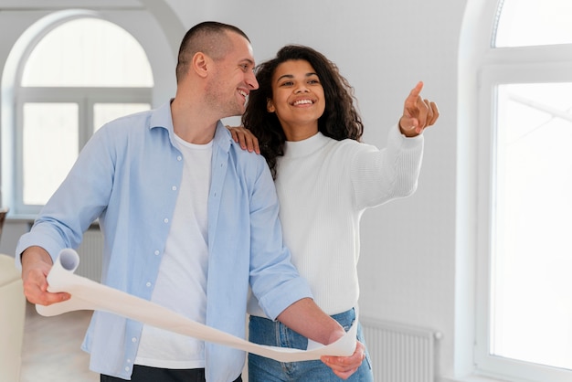 Pareja sonriente dentro de su nuevo hogar con planos de casas