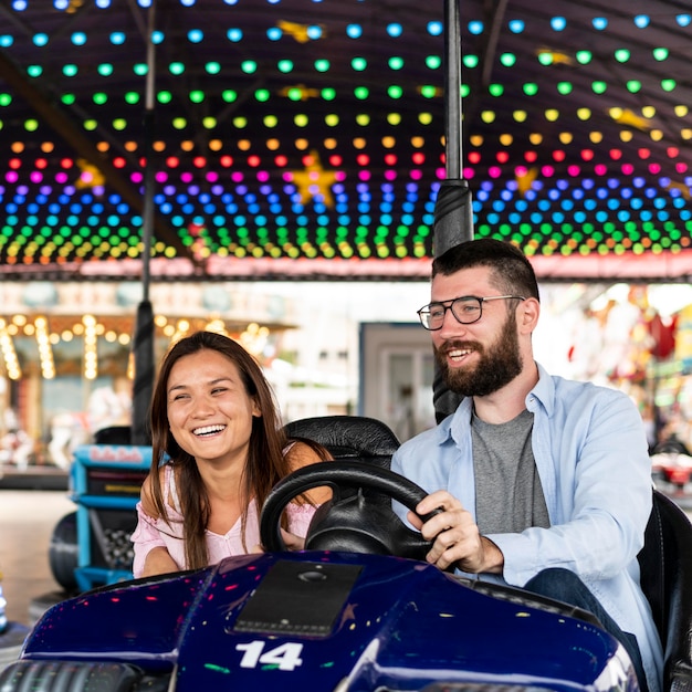 Foto gratuita pareja sonriente divirtiéndose con autos chocadores