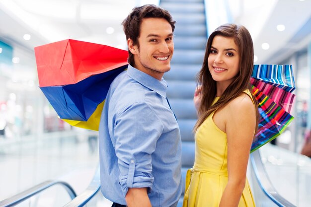 Pareja sonriente en escaleras mecánicas en el centro comercial