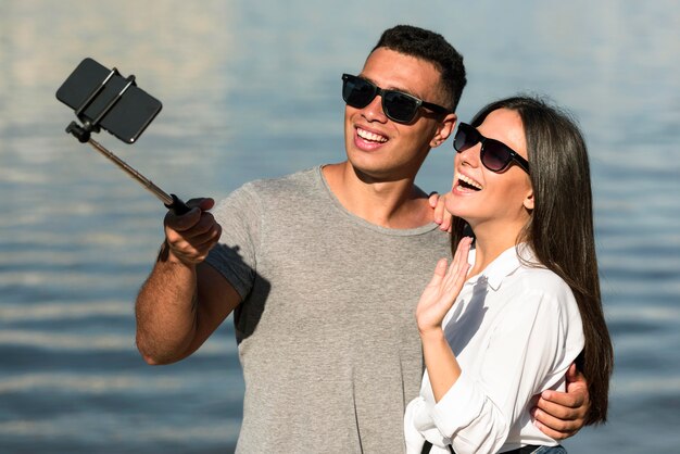 Pareja sonriente con gafas de sol tomando selfie en la playa
