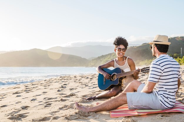 Pareja sonriente con guitarra en la playa