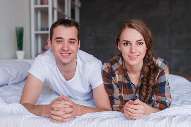 Pareja sonriente joven acostado en cama en casa