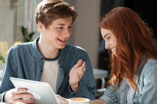 Pareja sonriente joven hablando mientras usa la tableta