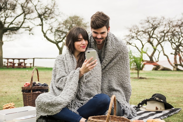 Pareja sonriente joven mirando el teléfono móvil en el parque