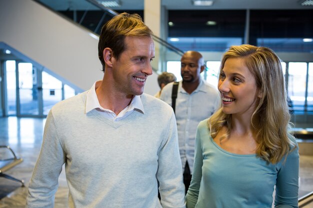 Pareja sonriente mirando el uno al otro mientras está de pie en la sala de espera