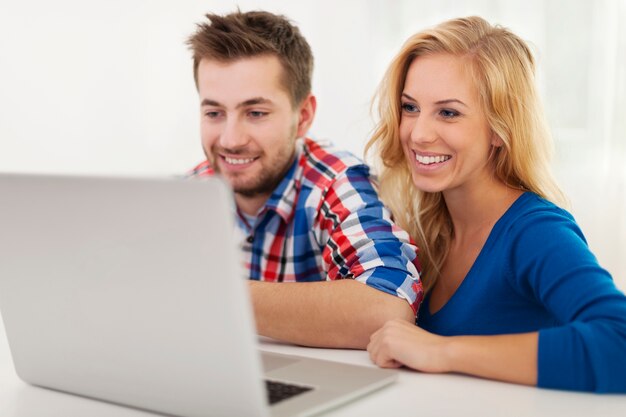 Pareja sonriente mirando en el portátil en casa