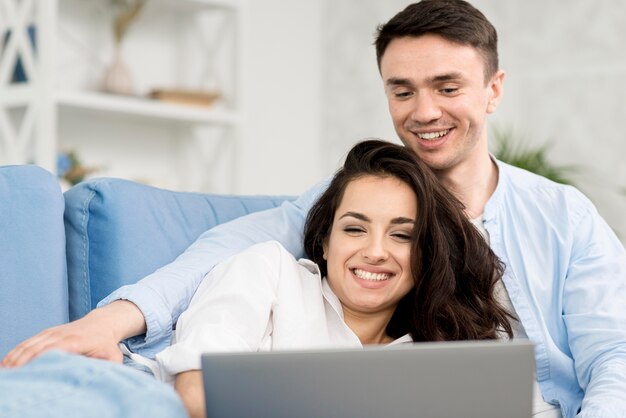 Pareja sonriente mirando portátil en el sofá