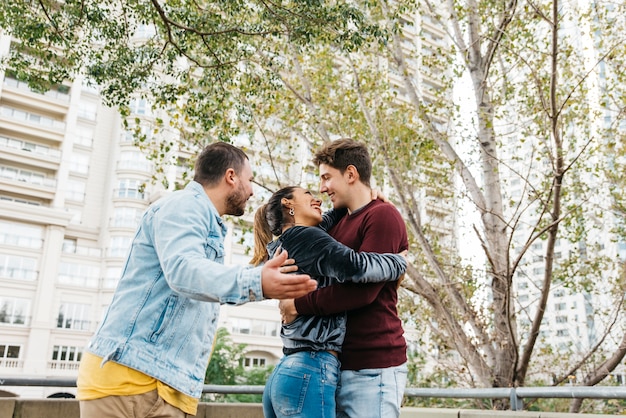 Pareja sonriente multirracial caminando con un amigo en la calle