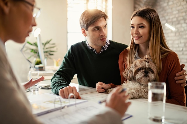 Pareja sonriente con un perro hablando con su agente de seguros durante una reunión en la oficina