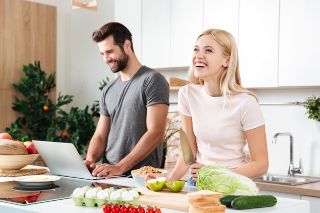 Pareja sonriente con portátil para cocinar en su cocina