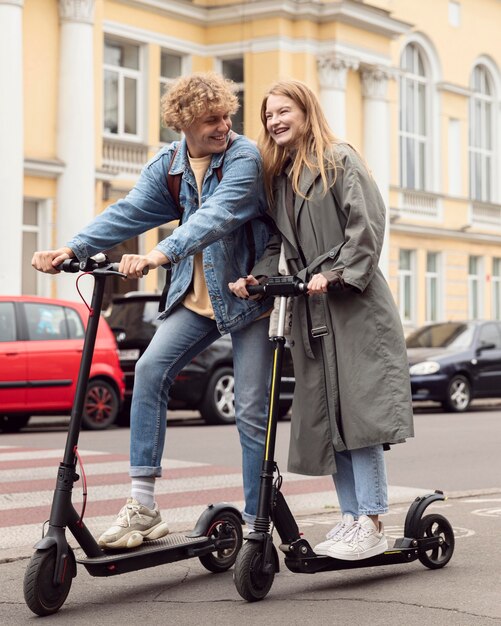 Pareja sonriente posando juntos al aire libre en scooters eléctricos