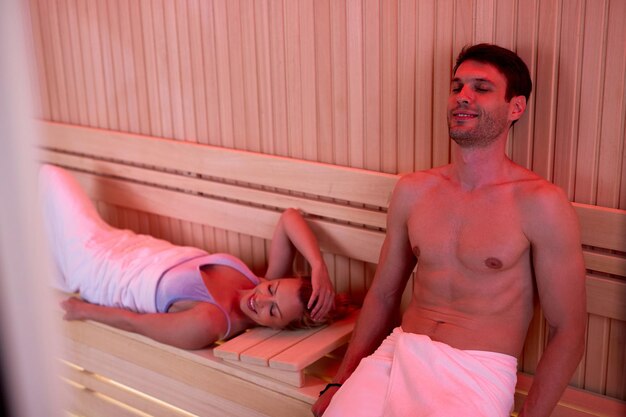 Pareja sonriente relajándose con los ojos cerrados en sauna en el centro de bienestar