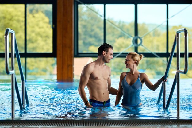 Pareja sonriente saliendo de la piscina termal y hablando mientras disfruta de un día en el spa