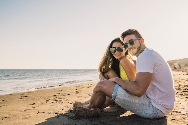 Pareja sonriente sentada por la playa