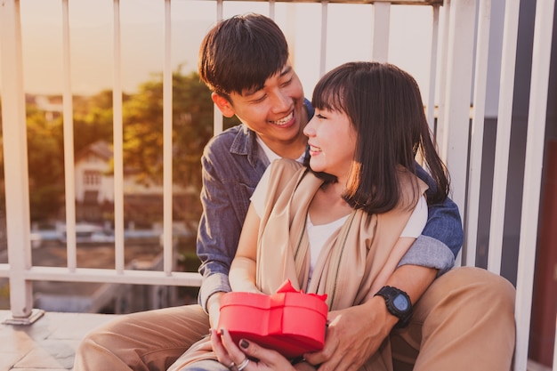 Pareja sonriente sentada en el suelo con un regalo rojo