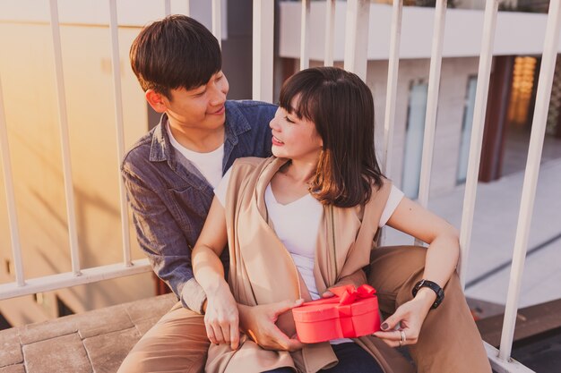 Pareja sonriente sentada en el suelo con un regalo rojo