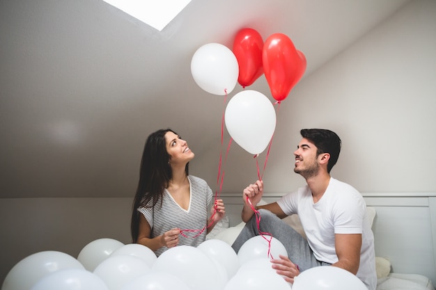 Pareja sonriente sujetando globos rojos y blancos