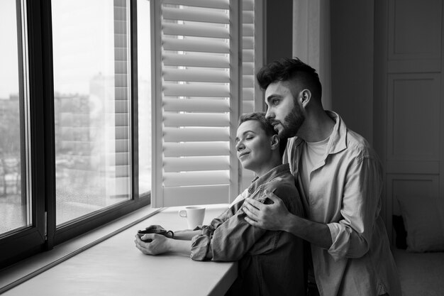 Pareja sonriente de tiro medio mirando por la ventana