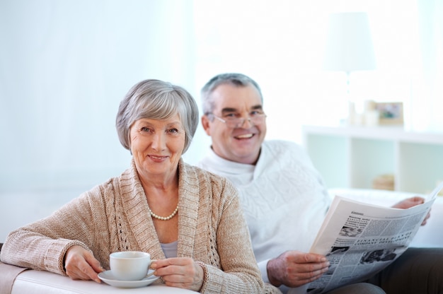 Pareja sonriente tomando café y leyendo el periódico