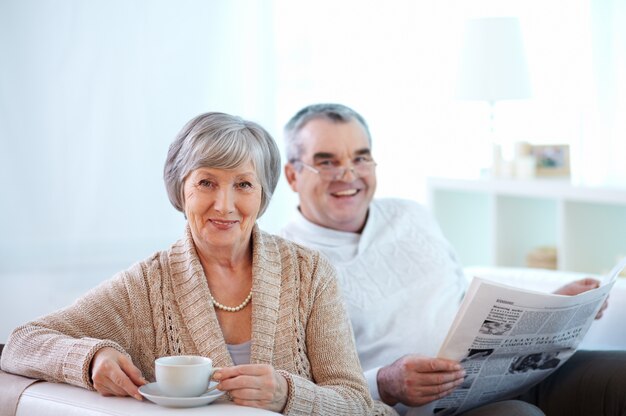 Pareja sonriente tomando café y leyendo el periódico